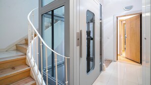 Een modern interieur met een spiltrap, een glazen lift en een houten deur.