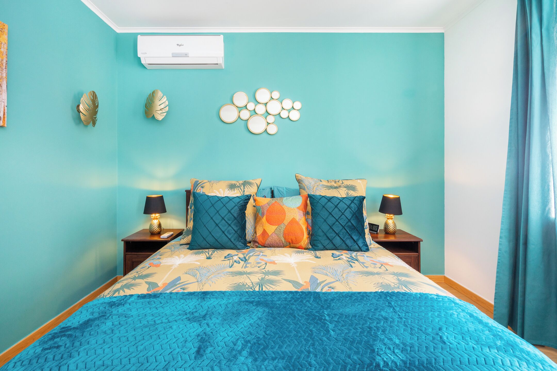 Un dormitorio con una cama, dos mesitas de noche, un aire acondicionado de pared y una decoración mural con temática tropical.