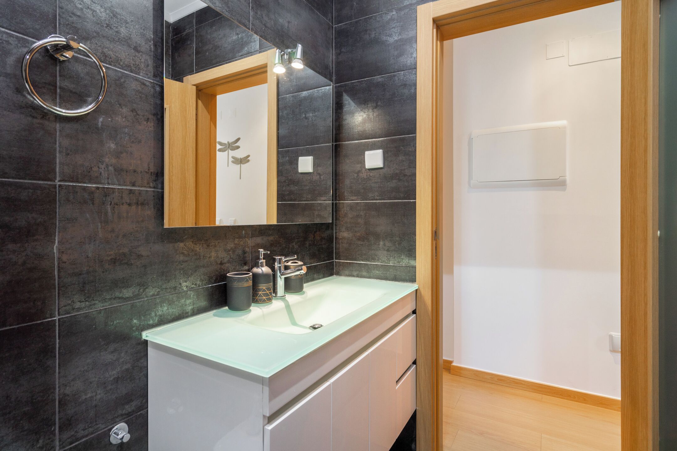 A modern bathroom with dark tiled walls, a white sink, and a wooden door.