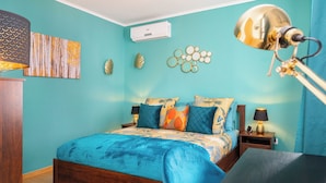 Een slaapkamer met een bed, nachtkastjes, een lamp, wanddecoratie en een airconditioner.