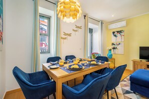 A dining area with a wooden table, blue upholstered chairs, and a hanging light fixture. - Premium Family Apartment W/ Lift, Ac & Barbecue (Lisbon)