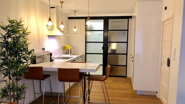 A modern kitchen with a central island, bar stools, pendant lights, and a sliding glass door leading to a dining area.