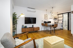 A modern living room with a flat-screen TV, wooden flooring, a dining area with a table and chairs, and a kitchen with a sink and countertop. - Green Street 1-Bed Perfect To Explore Lisbon (Lisbon)