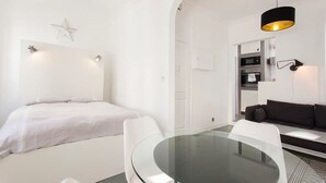 Ein modernes, minimalistisches Schlafzimmer mit einem Bett, einem Glastisch und einem dunkelgrauen Sofa.