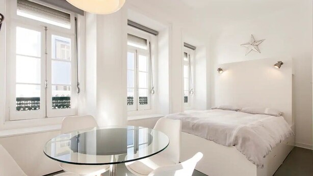 Ein modernes Schlafzimmer mit Glastisch, weißen Möbeln und einem Bett mit weißer Bettdecke.