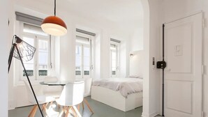 Ein modernes, minimalistisches Schlafzimmer mit einem Bett, einem Schreibtisch mit Stühlen und einer Hängelampe.