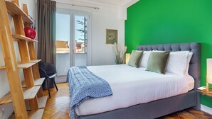 A bedroom with a large bed, a wooden shelf unit, a black chair, and a green wall.