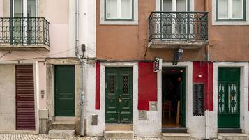Una hilera de edificios con puertas verdes y rojas, una calle empedrada y un balcón visible con barandillas de metal.