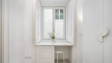 Una habitación blanca con ventana, un escritorio y un taburete.