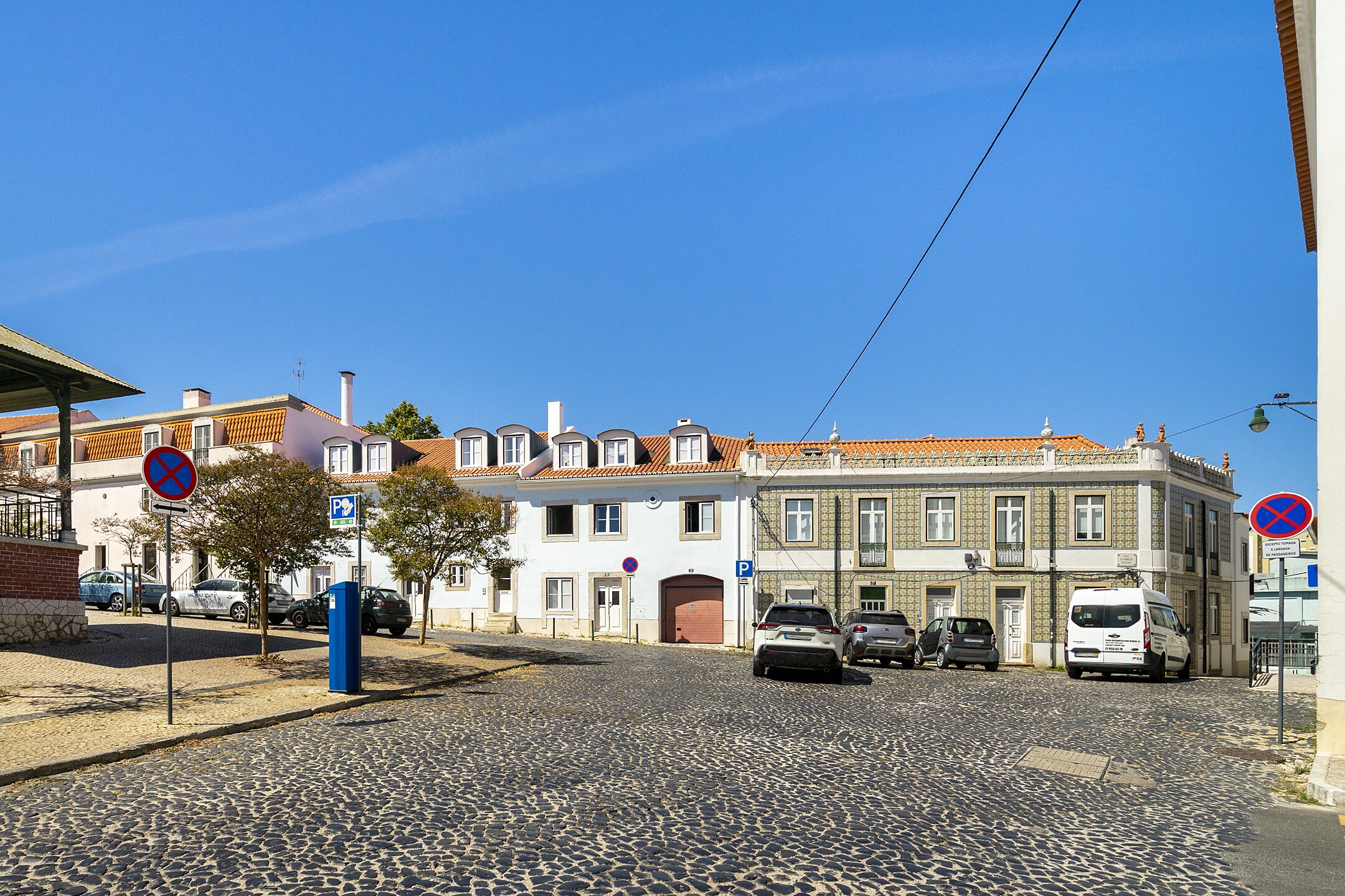A cobblestone street with parked cars and buildings with traditional architecture.