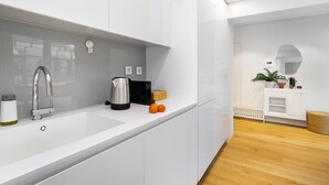 Una cocina moderna con armarios blancos, un lavamanos de acero inoxidable y una cafetera.