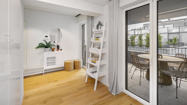 Un apartamento moderno con piso de madera, paredes blancas, una estantería blanca, un espejo y un balcón con mobiliario exterior.