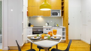 A compact kitchen with white cabinets, a microwave, and a dining table set for breakfast. - Dreamy Living Your Chic Graça Retreat (Lisbon)