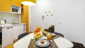 A modern kitchen with wooden cabinets, a microwave, and a sink. There is a dining table set with plates, cutlery, and a pitcher of orange juice. - Dreamy Living Your Chic Graça Retreat (Lisbon)