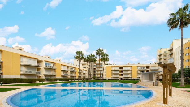 A swimming pool surrounded by multi-story buildings with balconies, palm trees, and a clear sky. - Family Holidays W/ S-Pool, Ac, Elevator & Garage (Loulé)