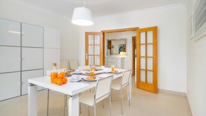 A modern dining area with a white table set for four, including orange juice and croissants. - Family Holidays W/ S-Pool, Ac, Elevator & Garage (Loulé)