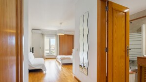 A hotel room with a wooden floor, a bed, a bathroom with a mirror, and a view of the city through the window. - Family Holidays W/ S-Pool, Ac, Elevator & Garage (Loulé)