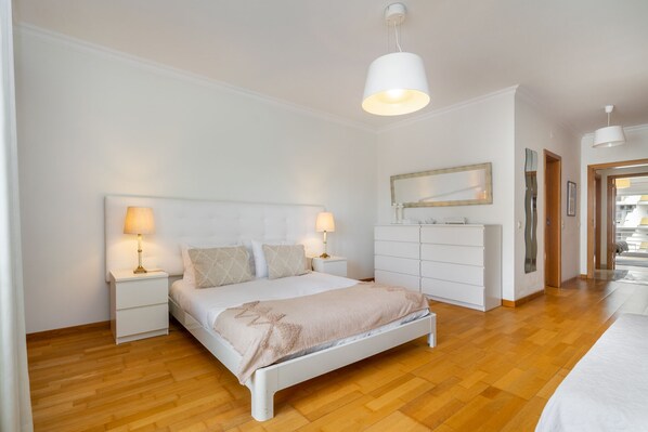 A bedroom with a white bed, two bedside tables with lamps, a dresser, and a mirror on the wall.