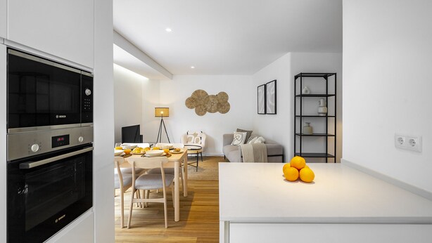 A modern kitchen with a Bosch oven, a dining area with a table and chairs, a sofa, and a shelf with decorative items.