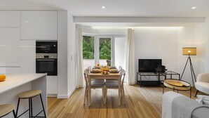 A modern kitchen with white cabinets, a dining area with a wooden table and chairs, a TV, and a floor lamp.