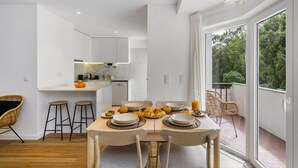 A modern kitchen with white cabinets, a dining table set with plates, bowls, and glasses, and a view of greenery through large windows.