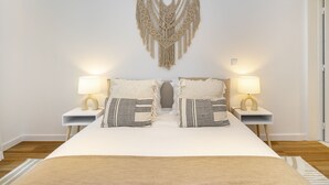A neatly made bed with two bedside tables, each with a lamp, and a macramé wall hanging above.