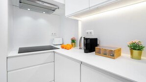 Une cuisine moderne avec des meubles blancs, un four encastré, une machine à café et un panier à fruits.