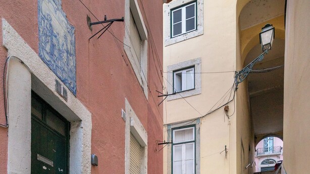 Un escalier étroit, avec des marches en pierre, mène à un bâtiment à la façade rouge et à la porte bleue.