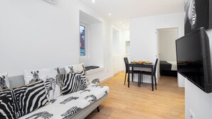 Un salon moderne avec un canapé à motifs zébrés, un coin repas comprenant une table et des chaises, et un téléviseur à écran plat fixé au mur.
