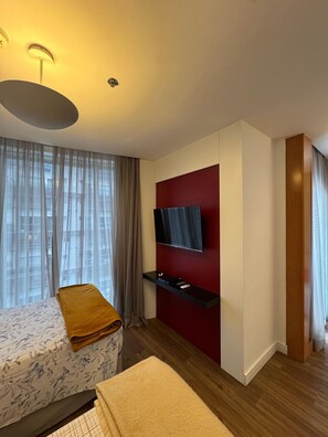 Una habitación de hotel moderna con una cama grande, un televisor montado en una pared roja decorativa y suelo de madera.