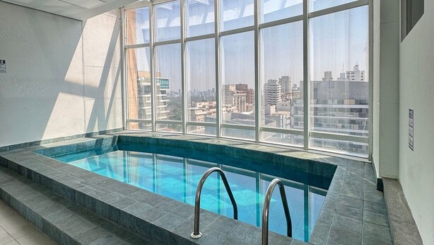 Piscina interior moderna con vistas a la ciudad a través de amplios ventanales.