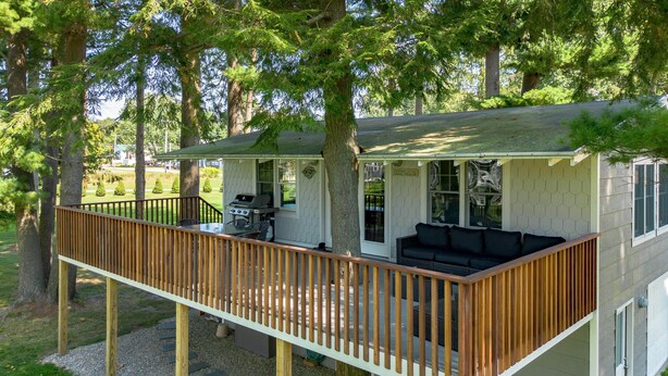 Une maison à deux étages avec une terrasse, un barbecue et un canapé.