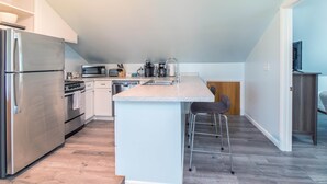 Une cuisine moderne dotée d’un îlot central, d’appareils électroménagers en acier inoxydable et d’un plancher à motifs en chevrons.