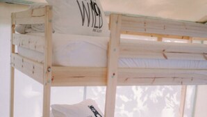 Ein Stockbett mit weißer Bettwäsche und Kissen, ein gemustertes Teppich und ein Fenster mit Blick auf Bäume.