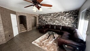 Amplia sala de estar con sofá modular, chimenea, ventilador de techo y pared de mármol.