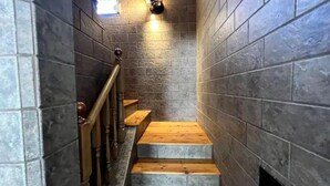 Una escalera estrecha con escalones de madera y barandilla de metal, flanqueada por muros de piedra.