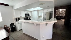 Una cocina moderna con armarios blancos, una isla central y un comedor con mesa y sillas.