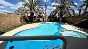 Una piscina con diseño curvo, rodeada de palmeras y una valla de madera.