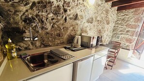 A kitchen with a stone wall, stainless steel sink, and a microwave. - Palheiro Jardim by Olá Madeira (Paúl do Mar)