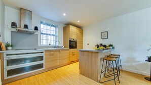 Una cocina moderna con armarios de madera, horno empotrado y una zona de bar con taburetes.