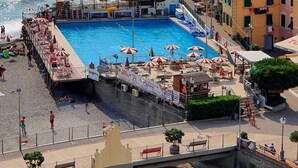 En havsnära pool med en brygga, omgiven av färgglada byggnader och med en fri utsikt över havet.