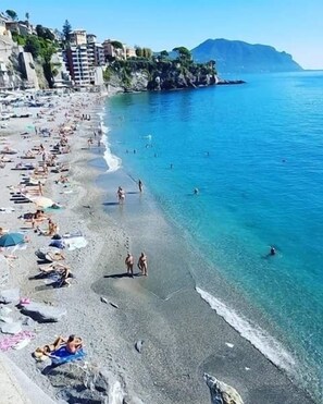 A beach with clear blue water, people sunbathing, and buildings in the background.
