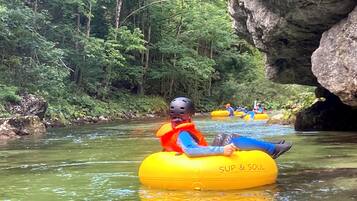 A person in a yellow inflatable tube with "SUP & SOUL" written on it, floating on a river surrounded by greenery and rocks.