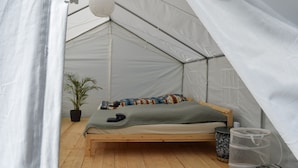 Ein Zeltraum mit Bett, Topfpflanze und Aufbewahrungsbox.