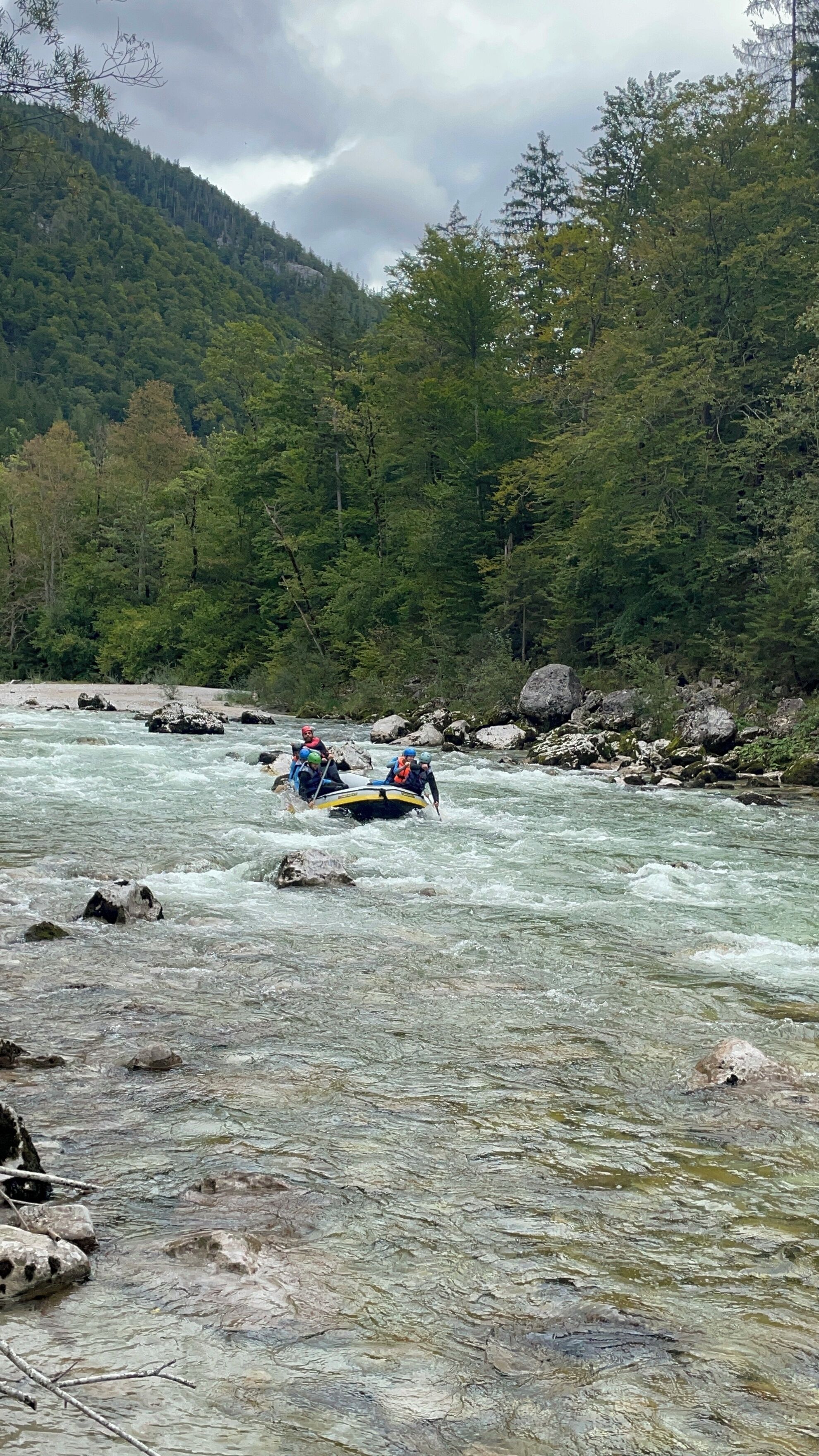 Een groep mensen die op een raft een rivier afdaalt, omringd door beboste heuvels.