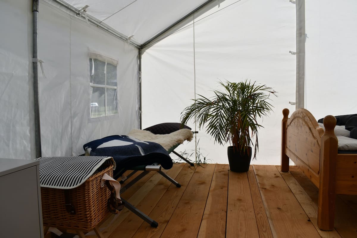 Una habitación con carpa, una cama, una mesita y una planta en maceta.