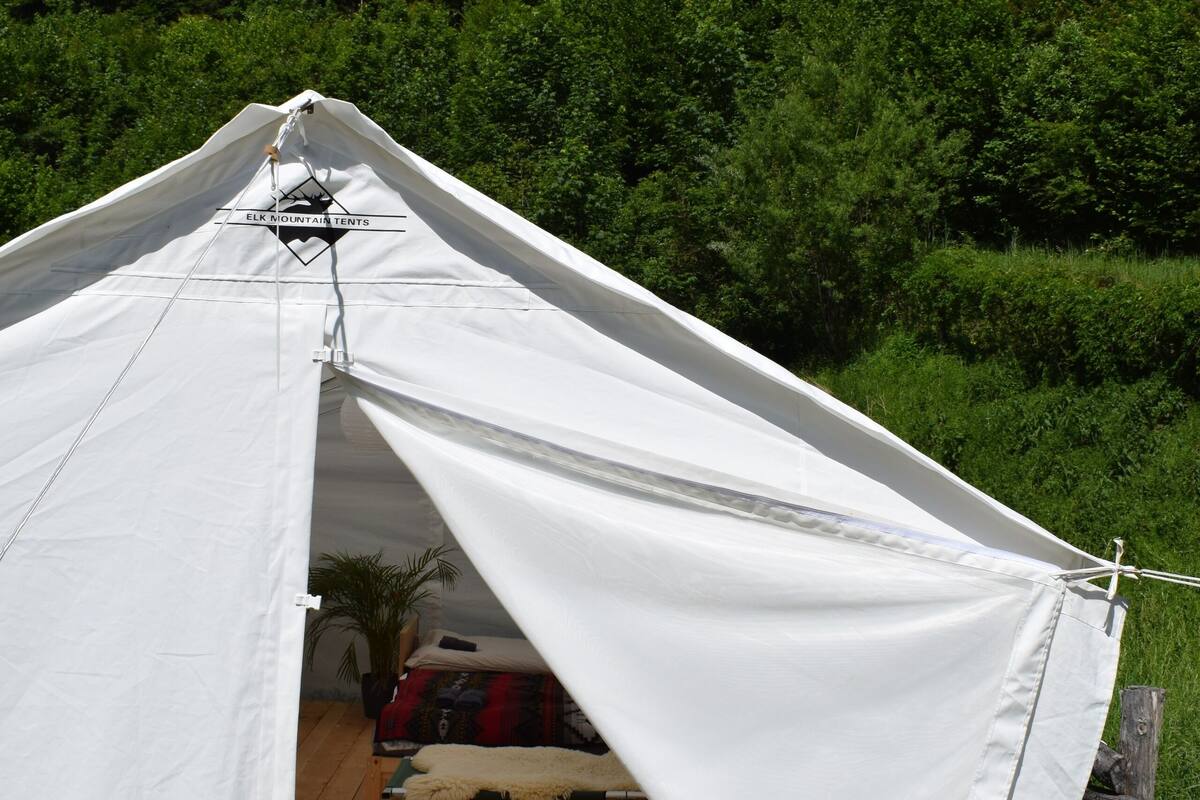 Una carpa blanca con un logotipo, montada sobre una plataforma de madera con vistas a una ladera boscosa.