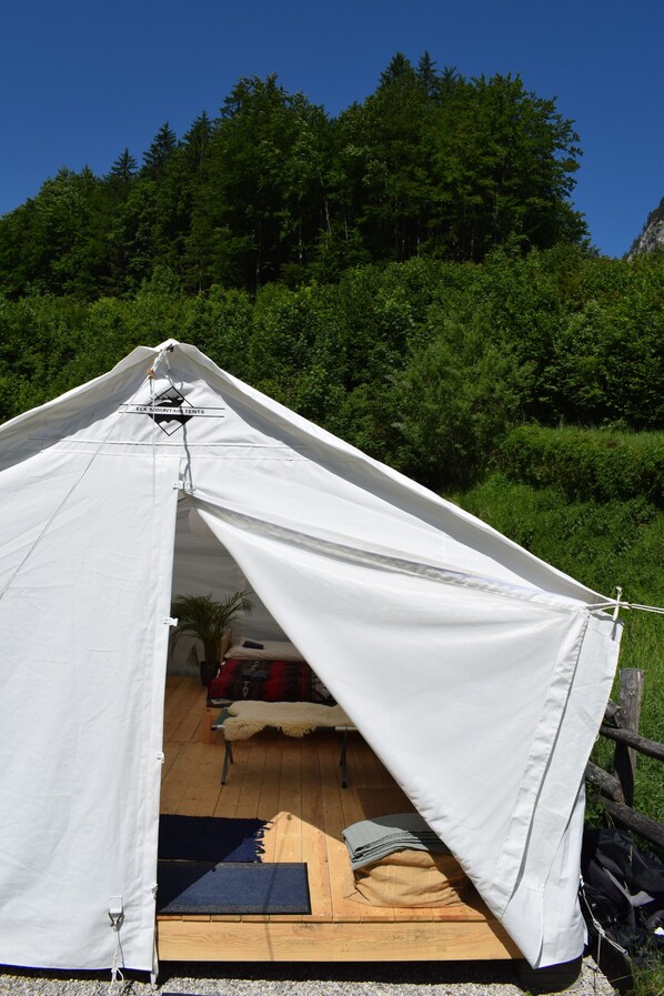 A white tent with a logo, set up on a wooden platform with a view of a forested hillside. - Wild Glamping in the Vienna Alps (Schwarzau im Gebirge)