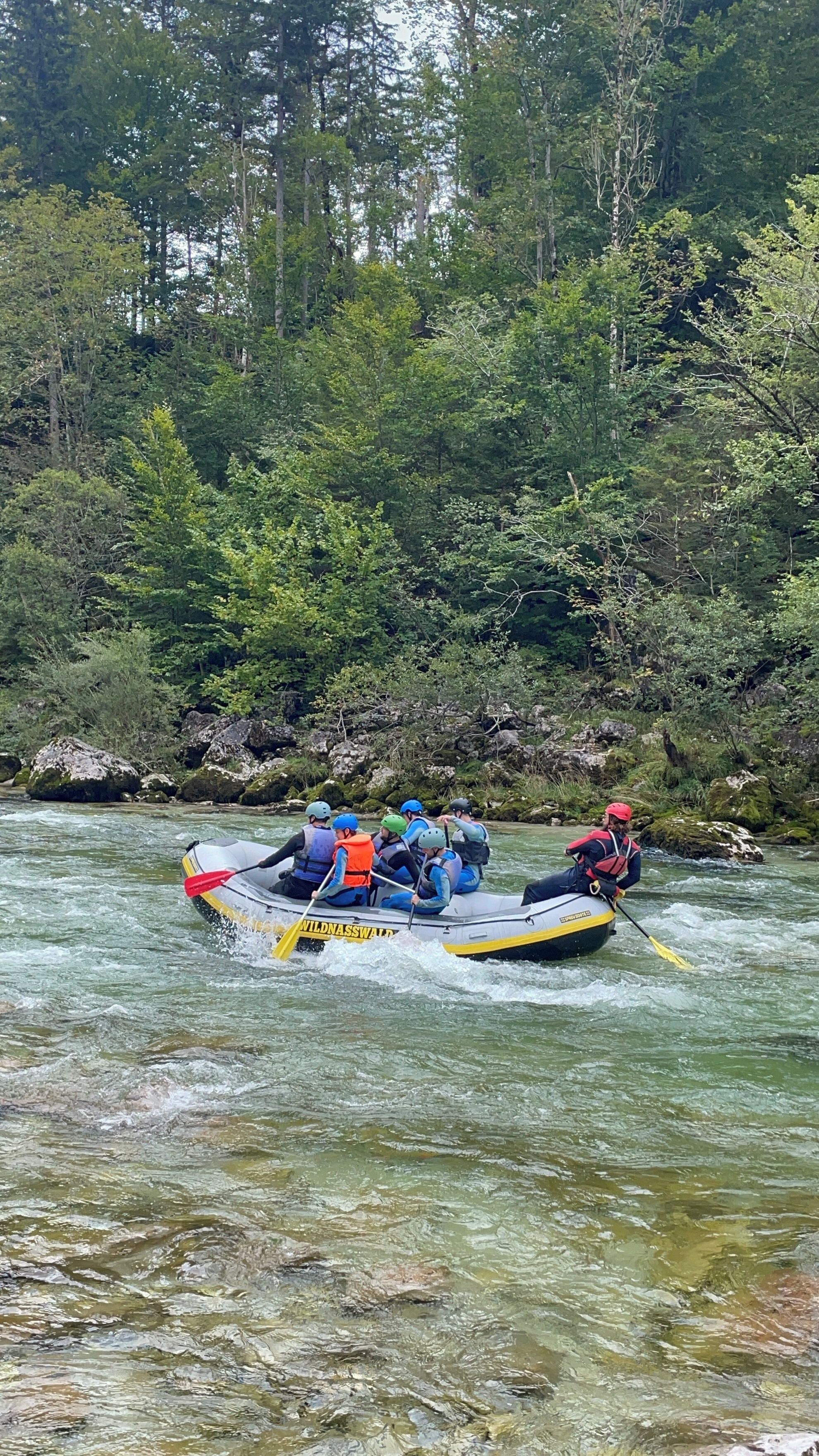 A group of people in a raft navigating a river surrounded by dense forest.