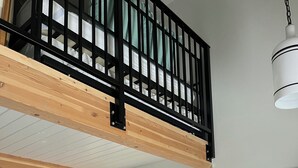 Un dormitorio con cama altilocta, una mesita de noche con lámpara, un cuadro enmarcado y una planta en maceta.